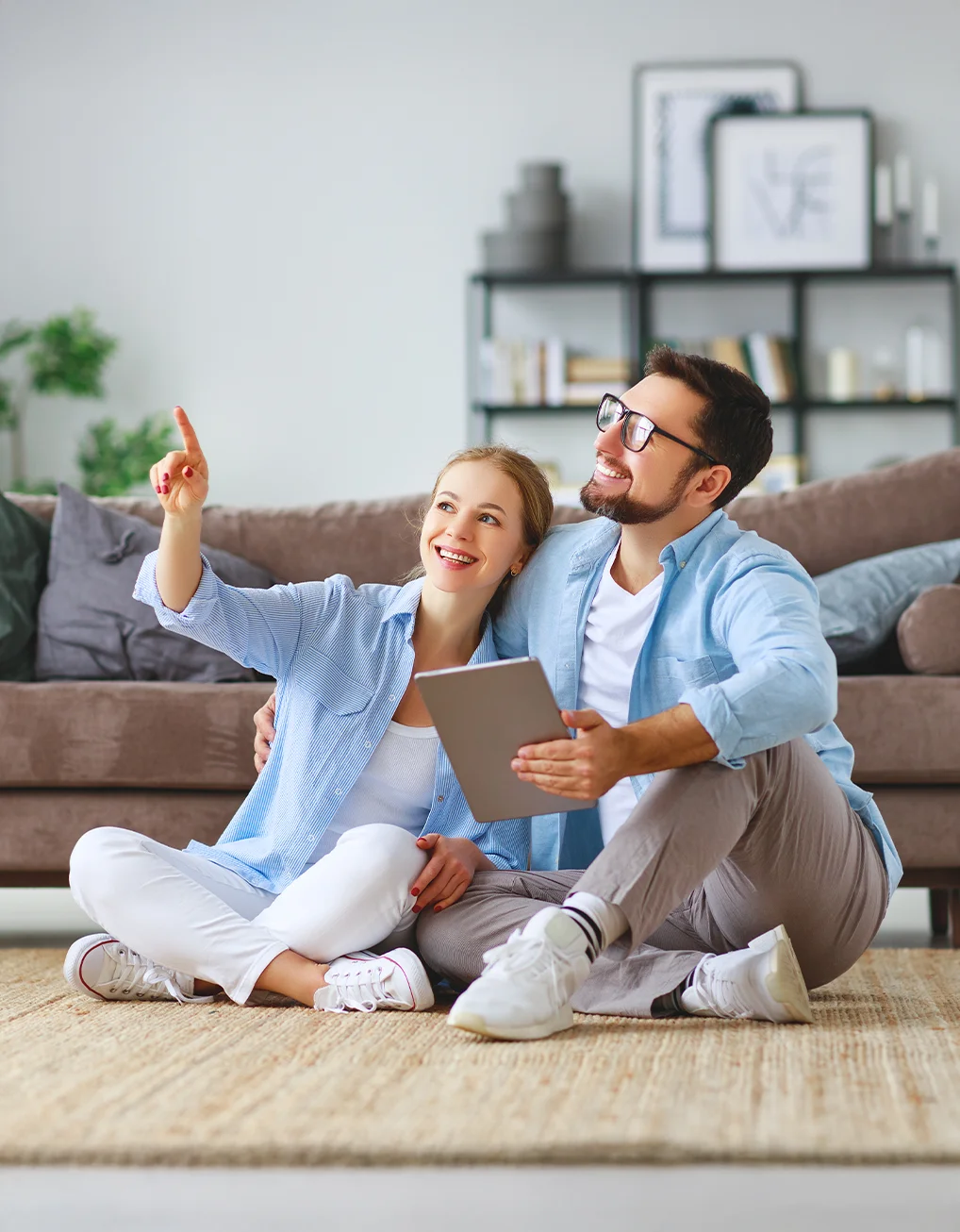 Young married couple sat inside their home holding an electronic tablet